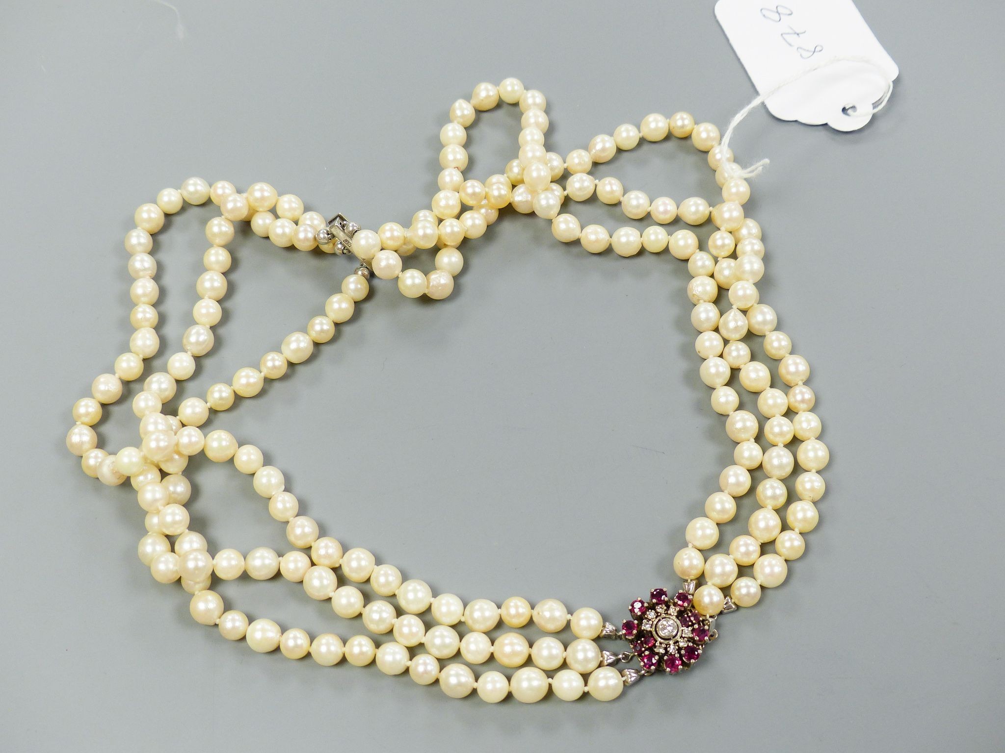 A triple strand cultured pearl necklace, with 585 white metal, ruby and diamond cluster set central motif and 585 white metal clasp, approx. 48cm, gross weight 104.6 grams